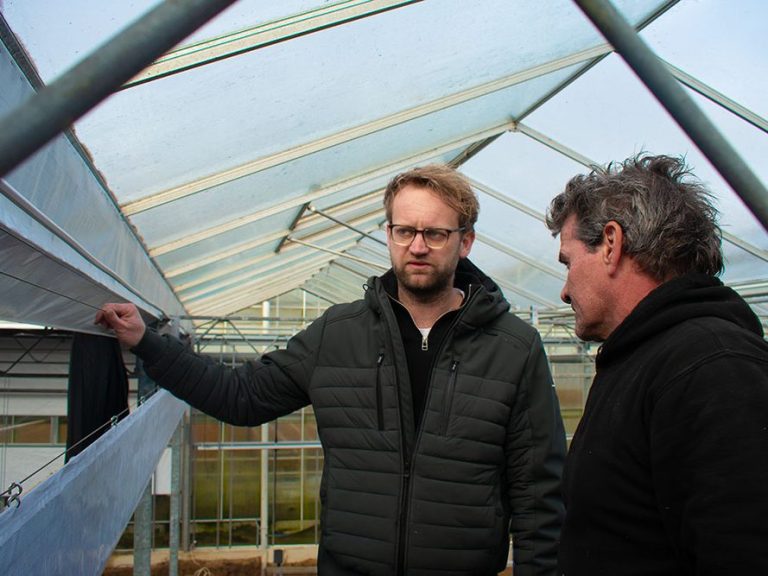 Robbie van den Ende met een glimlach, gekleed in een witte blouse, staand voor een van zijn projecten.